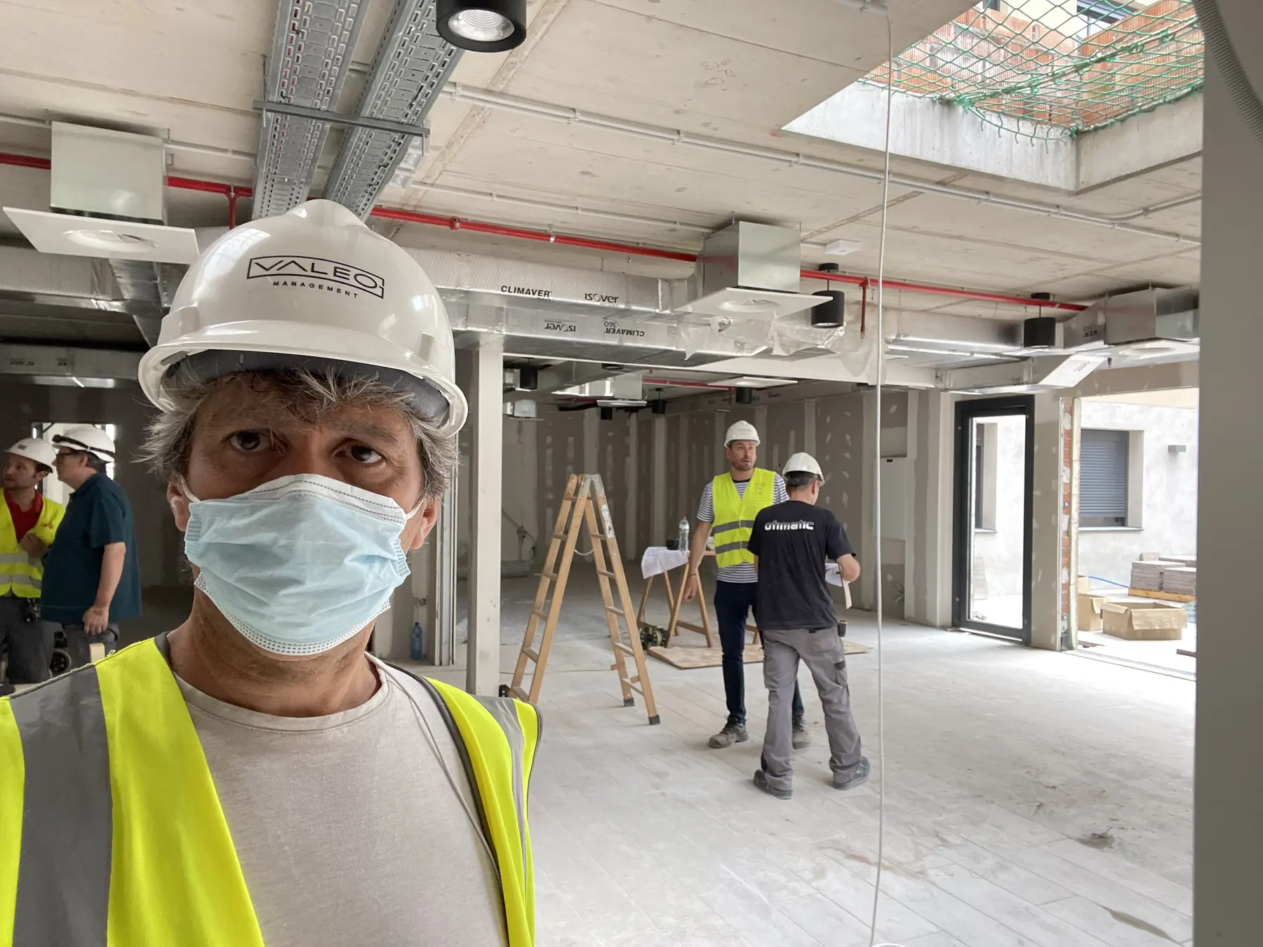 Project lead and construction team in an unfinished residence room, wearing hard hats and high-visibility vests