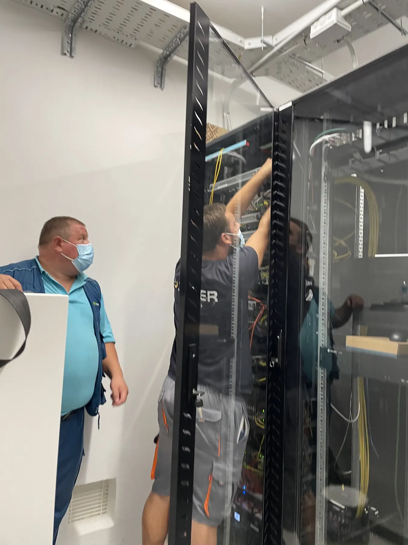 A technician working inside an equipment rack while another person stands beside it