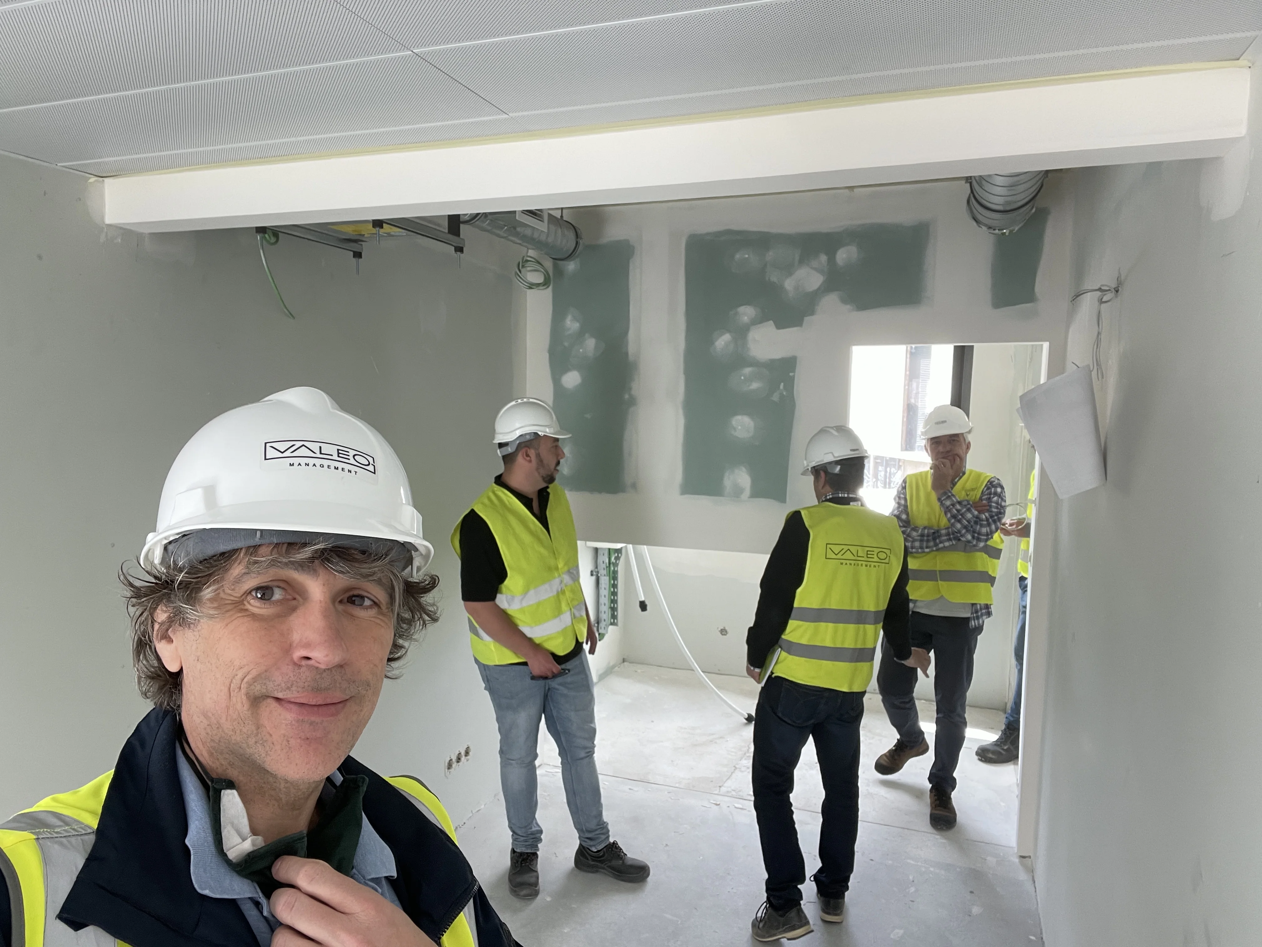 Project lead and team members in high-visibility vests and hard hats inside an unfinished room