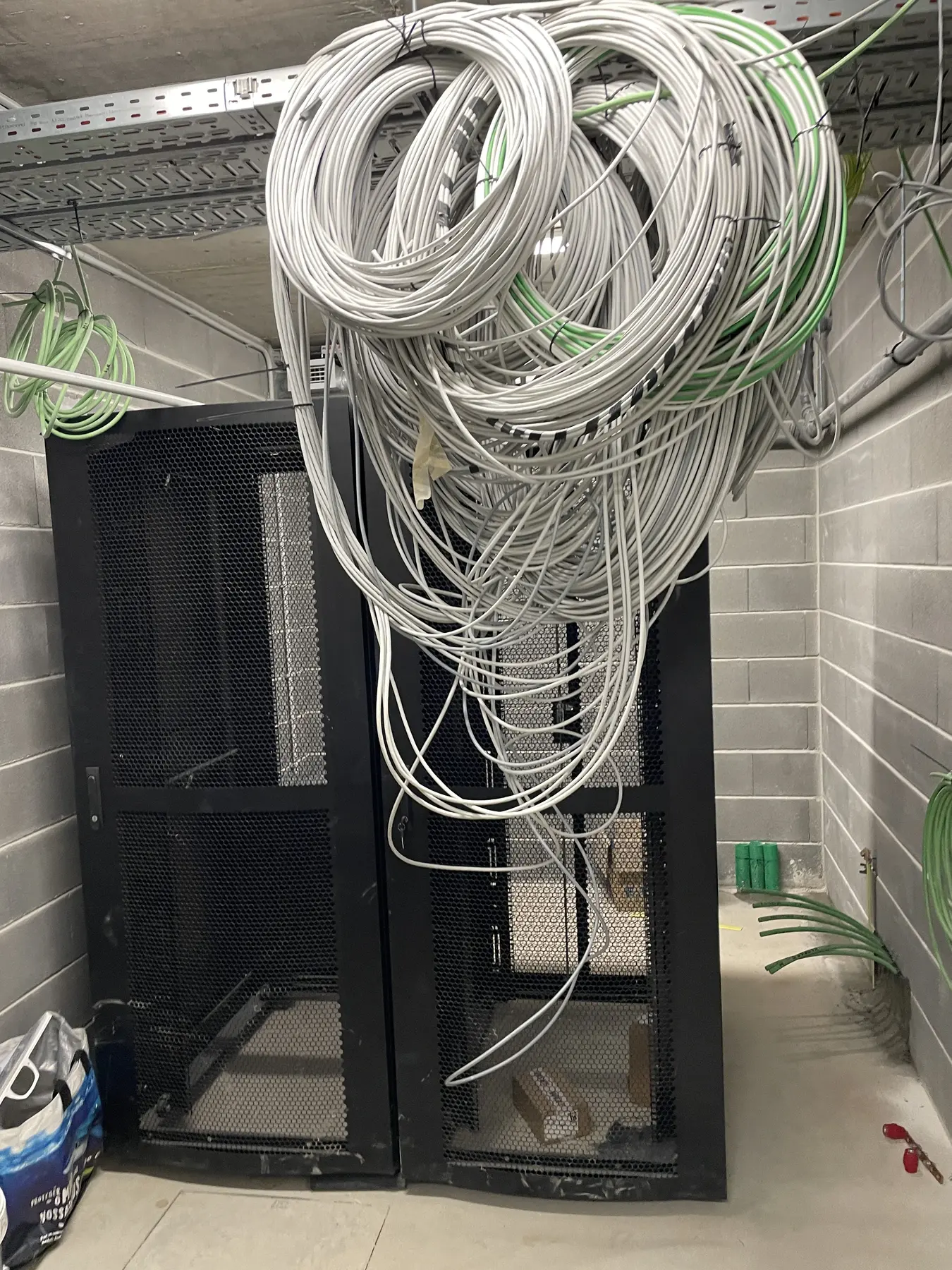 Coils of white and green cabling above a black equipment rack in a tiled room
